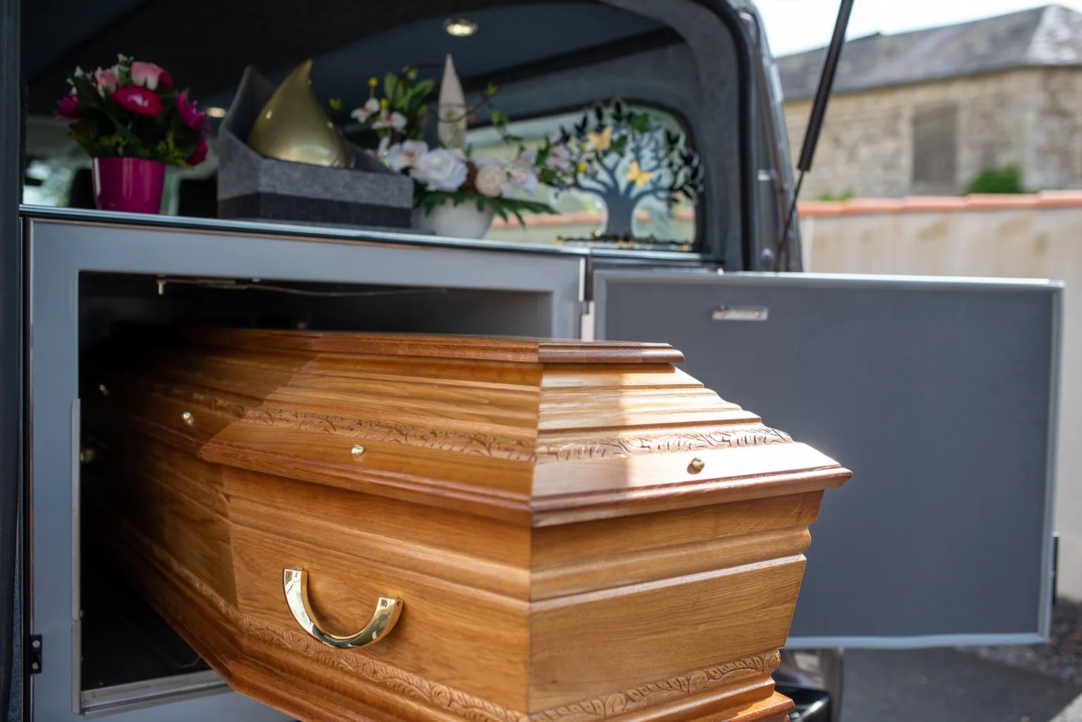 Corbillard de pompes funèbres chargé d'un cercueil en bois et de fleurs